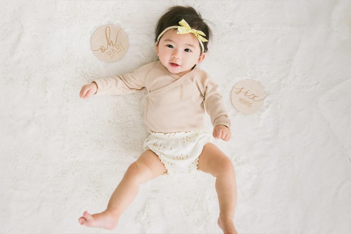 A baby lays on sheepskin with wooden mileston cards next to her.